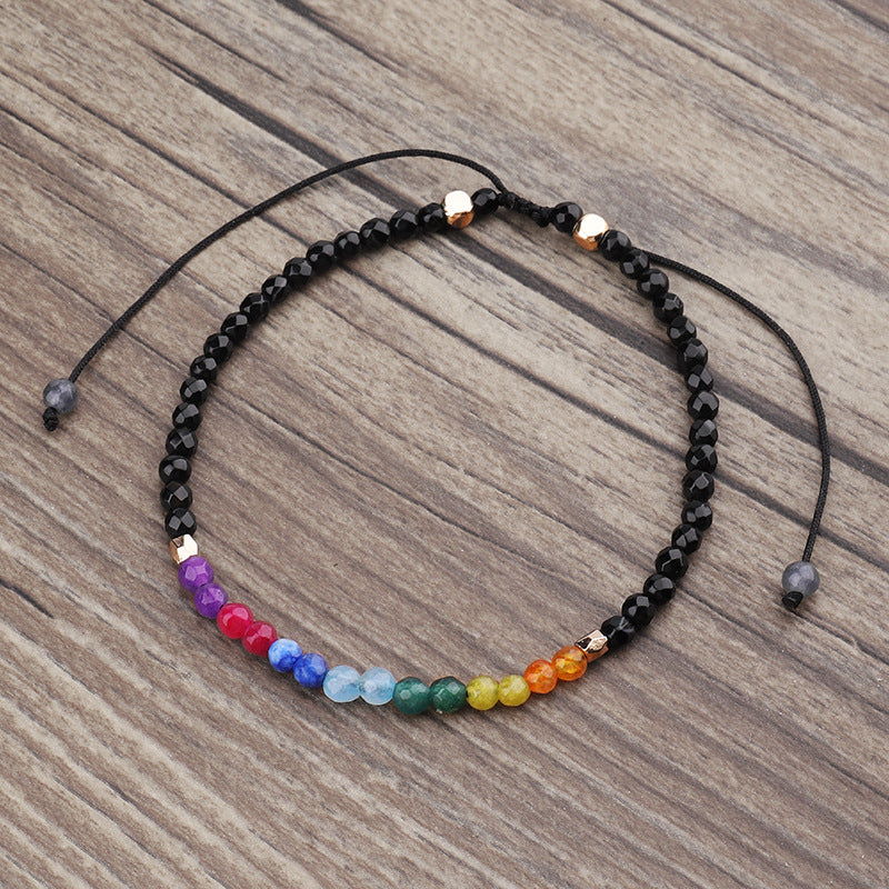 Seven chakras colored stones bracelet on wood, dark beads with rainbow center beads
